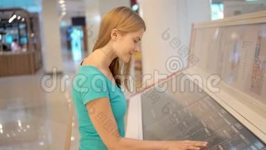美丽的年轻女子穿着绿松石T恤在商场。 在商场布局上寻找特定的商店